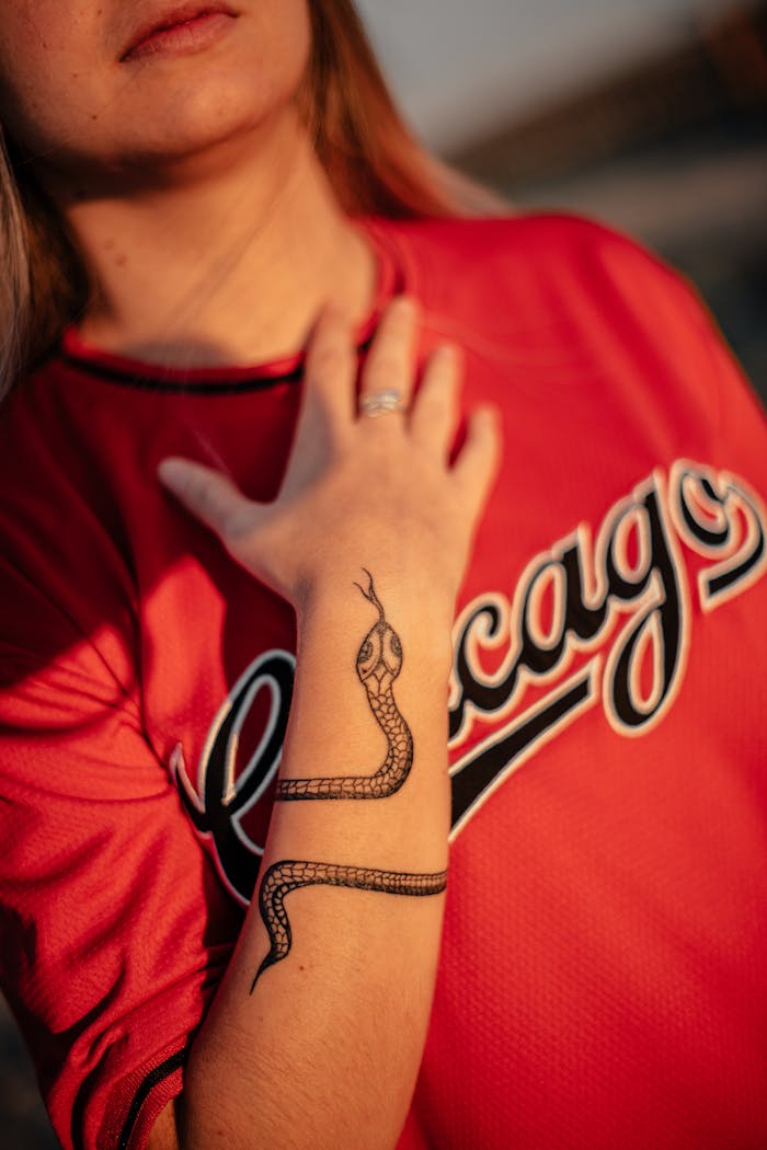 A woman with a snake tattoo on her arm, wearing a red Chicago shirt in warm lighting.