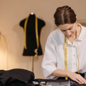 A fashion designer measuring fabric with a tape measure in a design studio setting.